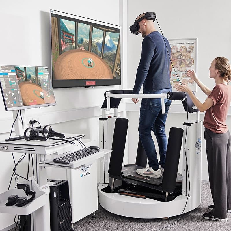 En audiolog hjælper en patient med en balance- og genoptræningsøvelse med BalanceVR-udstyr på MotionVR-platformen.